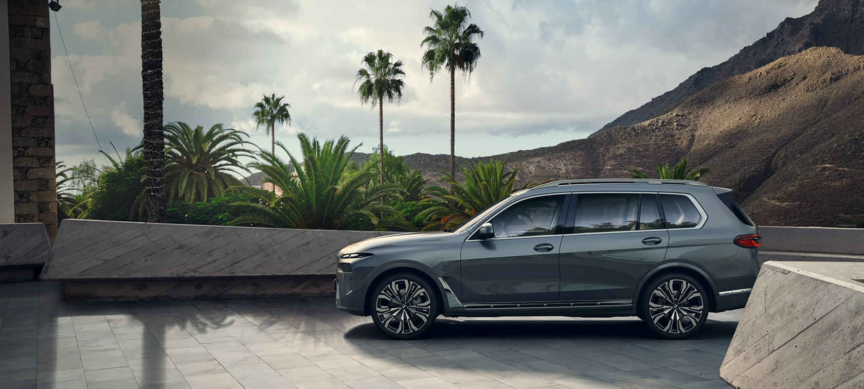  BMW X7 G07 LCI vue de profil à l’arrêt devant des arbres Sparkling Kupfergrau metallic